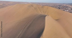 Desert sand dunes and city town of Peru. Close to Ica and Huacachina. Similar to Sahara and Emirates Deserts. Boogie cars driving and people sandboarding. Aerial drone high resolution 4k