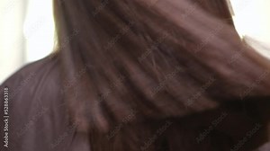 Close-up brunette laminated hair shaking in slow motion indoors. Back view unrecognizable Cauacsian satisfied woman doing hair toss in beauty salon