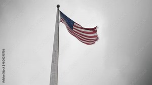 American flag blowing in the wind. A United States of America flag in front of grey sky blowing in slow motion.
