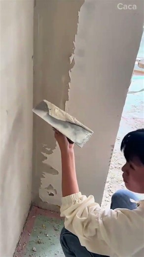 Scraping and peeling off old damaged paint layer from a concrete wall using a metal trowel tool
