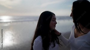 mid adult latina mother and teenage daughter on the beach chatting and getting their hair done