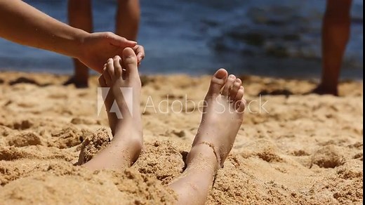 Child, tickling sibling on the beach on the feet with feather, kid cover in sand, smiling, laughing, enjoying some fun