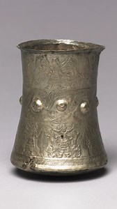 At least 2,700 years old, this hero and animal combat beaker is attributed to the Luristan culture of ancient Iran. It was made of silver using repoussé and engraving techniques, and features two registers depicting bearded men in long robes and scarves grasping and stabbing rearing beasts amid stylized trees. Along with guilloche patterns and round bosses separating the scenes. The beaker measures 10.1 cm (4 in) in height with a diameter of 7.7 cm (3 1/16 in). This artifact is now housed by the