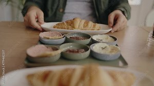 Cropped view on man eating fresh croissant in cafe for breakfast. Waiter bring plate with crispy croissant and ingredient for filling, cheese, spread and sauce