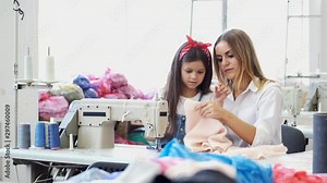 Girls are sewing in garment studio. The mother teaches girl. The sewing machine is white.