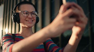 Attractive Carefree female share her current mood with followers on social media through video of herself. Woman in headphones use popular mobile app to enhance her selfie with filters and effects