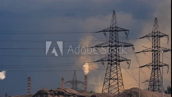 High voltage power lines and smoke stacks emit smoke against a dark, stormy sky. Industrial scene with environmental impact