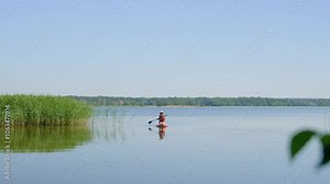 A woman paddling a SUP board along the river. SUP surfing. A young woman paddle boarding.