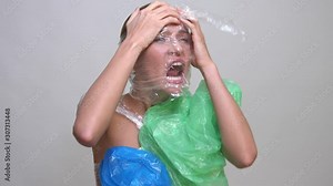 A terrified woman wrapped in plastic trash. Over grey background. No plastic and zero waste concept.
