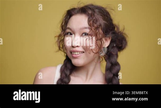 Portrait of a joyful young Kazakh woman with braided hair, showcasing cheerful expressions against a yellow background in a studio setting Stock Video Footage - Alamy