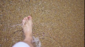 Barefoot person walking on the beach with waves washing over feet in 4k slow motion 120fps