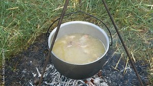 A woman cooks soup on a fire, stirs it with a ladle, a girl bakes potatoes put on a stick.