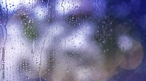 4k : Close-up of rain drops splashing against a window glass with light bokeh and light leaks.