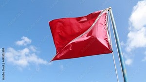 A red and white scuba diving flag flapping in the wind, isolated, with a diagonal stripe attached to flag pole against bright blue sky with clouds, Barbados, Caribbean. Sport, recreation symbol