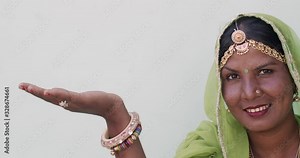 Close-up portrait of attractive Indian woman wearing traditional jewelry, green sari, head covered with dupatta sheer fabric, hand raised sideways for product placement for advertisement copy space