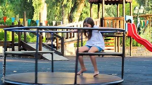Two little girls in the playground, having fun on a merry-go-round on a hot summer day