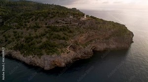 4K Aerial Drone video of popular summer destination, sunset over the cliffs with a lighthouse and a huge port of boats anchored at golden hour with seagulls flying. Port de Soller, Mallorca