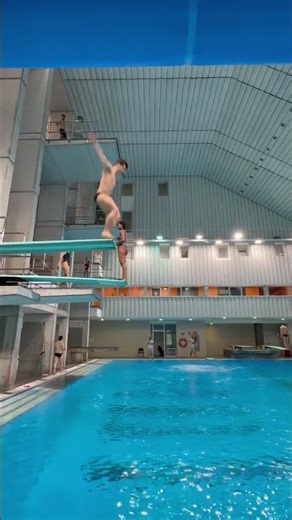 Diver Executes Advanced Dive from Springboard at Indoor Pool