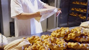 A bakery worker packs rolls into paper bags. the baker prepares orders for customers with rolls and whole dough products. Work process in a bakery with dough products. Successful family business