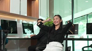 Happy employee female spins in chair, celebrating business deal, spinning around in chair, suddenly raising hands up in joy and spinning while sitting on a chair in an office, working on the computer.