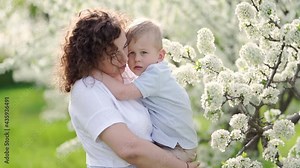 mother holds her young son in a flowering spring garden. parental love and care