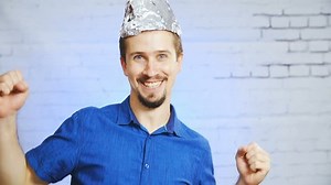 The tin-foil hat person mocking the stereotypes meme HD. Static portrait shot of a man in focus wearing a blue elegant shirt. Shoot on the bricked wall background with blue light.