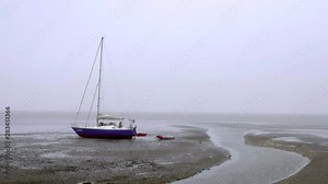 Small solitary sailboat stranded on the coast at low tide on a foggy day