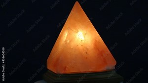 The orange salt lamp made of natural crystalline rock salt in the shape of a pyramid rotates on a dark background, acts as a tonic anti-stress source, health relax.