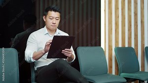 young asian male in waiting room for job interview or meeting. Thoughtful employee man holding folder paper while sitting at chair fills out a resume questionnaire in office.