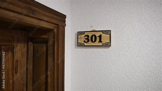 Stylish wooden carved hotel room sign on wall next to front door. Room number 301, sign for hotel, hostel, or residential complex. Elegant wooden door sign. Hotel business concept