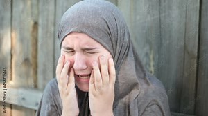 a teenage refugee girl is crying and screaming, holding her head in her hands, screaming in pain.