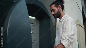 Man using debit card at ATM for cash withdrawal. male bank customer focused on transaction entering security password, showcasing daily banking activity. secure financial service