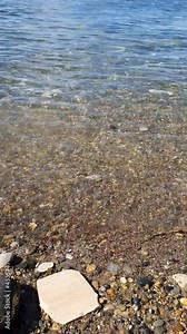 Clean sea water with ripples shore of stones, pebble beach