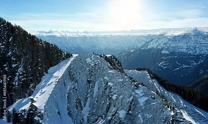 drone flight alpine summit ridge natural rock texture snowy hilly valley with sunny sky picturesque landscape. Aerial view winter mountain epic scenery high cliff peak freeze glacier slope