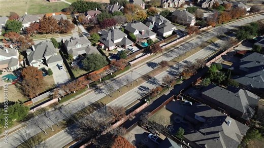 Dense grid of Coppell homes with pitched roofs and fenced yards, pools. Autumn trees in various stages of color change line sidewalks, parked cars and clean driveways completing suburbs view, TX