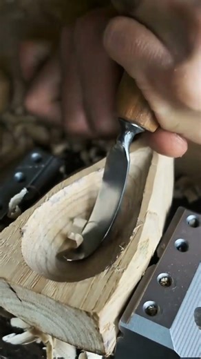 carving a wooden spoon using a curved gouge tool to hollow out the bowl with great precision