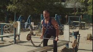 Brutal muscular bodybuilder doing heavy deadlift exercise at outdoor gym. Concentrated athletic fit man pumping up muscles with barbell, practicing upright row weight training during outdoor workout.