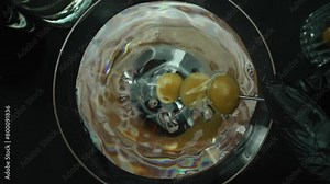 Top down view of skilled bartender hand prepare martini garnished with olive. Close up of hand making transparent cocktail drink with olive with movement and black background. Macrography. Comestible.
