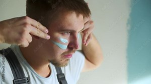 Builder man paint on his face battle color to paint the walls in the apartment or house. Construction, repair and renovation.