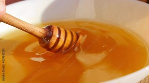 Honey is poured from a honey spoon into a plate. Freshly squeezed honey sparkles in the sun.