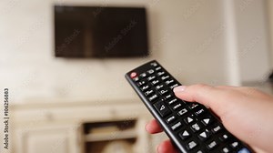 Hand holding TV remote control and changing channels on television.