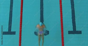 Professional athlete swims in dolphin style, training a swimmer in the pool. Woman swimmer is exercising in the pool, aquatic dolphin swimming style. Large pool with blue water and swimming lanes. 4k