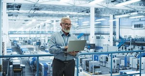 Electronics Manufacturing Technician Working on a Laptop Computer at a Factory Space. Specialist Developing, Maintaining, Fine-Tuning Programs for Machine Production and Assembly