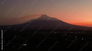 4K aerial footage of the beauty of Mount Merapi when the sky is still dark before sunrise. The panoramic beauty of Mount Merapi from a distance with a reddish sky in the background