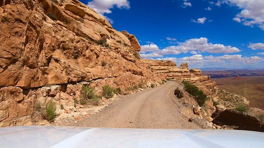 Moki Dugway. The Moki Dugway is a famous 3-mile, unpaved gravel road on Utah State Route 261, known for its steep switchbacks that climb nearly 1,200 feet up the side of Cedar Mesa. Carved by a mining company in the 1950s to transport uranium, this rugged road offers thrilling drives and breathtaking panoramic views of the Valley of the Gods and Monument Valley, but is not recommended for RVs, trailers, or in bad weather due to its narrow, guardrail-free sections. Please note all photos, videos