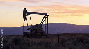 Silhouetted oil pump rig operates at sunrise in Vernal Utah oil field
