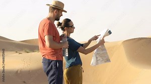 Young couple checking map, drinking water and walking on desert
