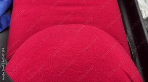 mom-to-be, wearing a red dress, seating in car with seat belt on and baby kicking and moving inside pregnant belly while riding in the car