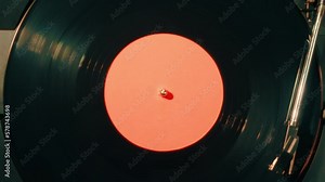 Close-up of a vinyl record with a orange sticker spinning on a retro turntable from top view. Black retro vinyl record on an old player. Close-up of a rotating plate on a player