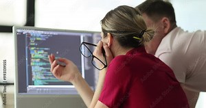Woman shows program coding on computer monitor to man colleague in office. Partners examine coding errors and bugs on computer screen slow motion